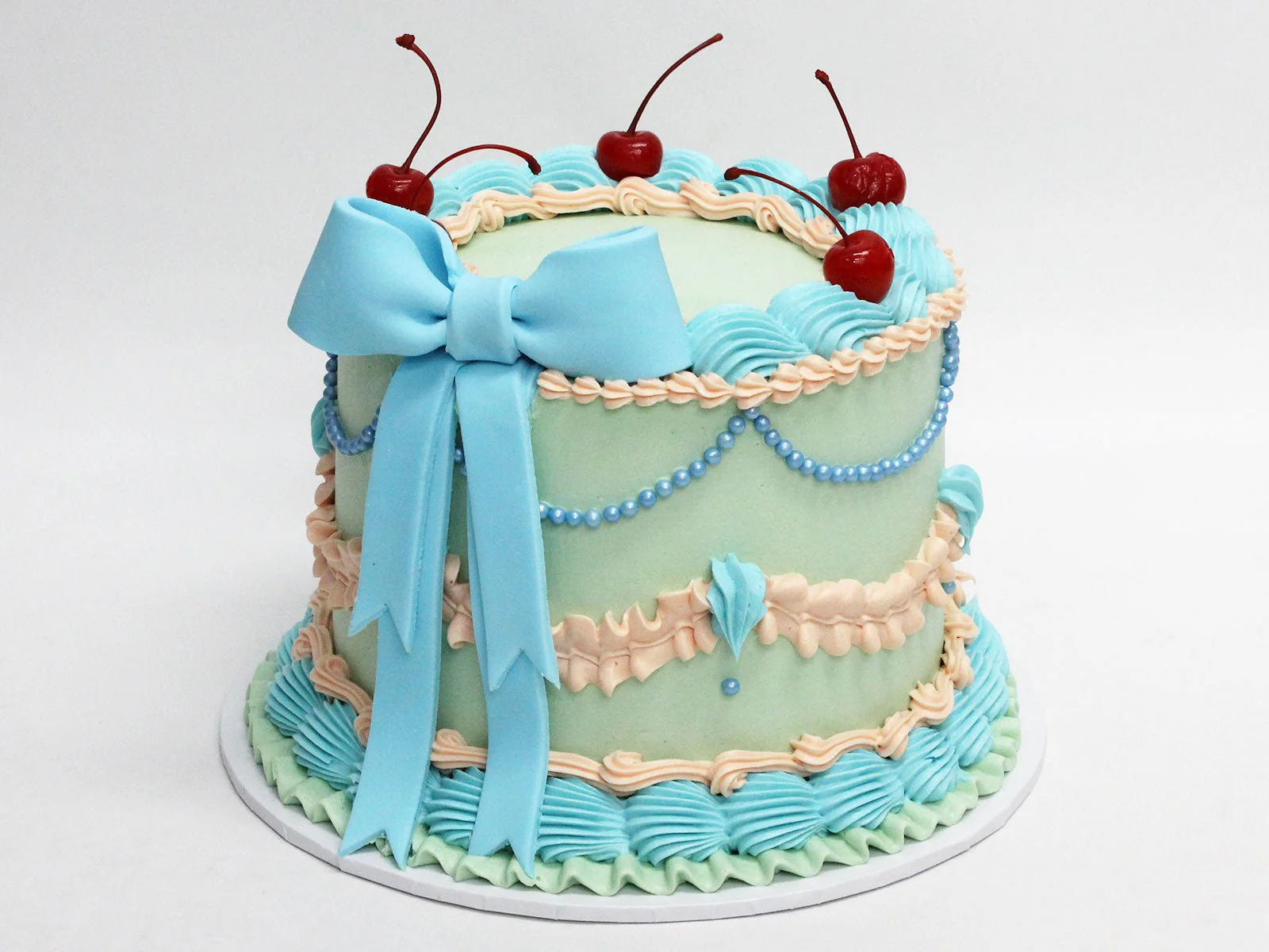 Blue round vintage cake with piped buttercream, cherries and a bow