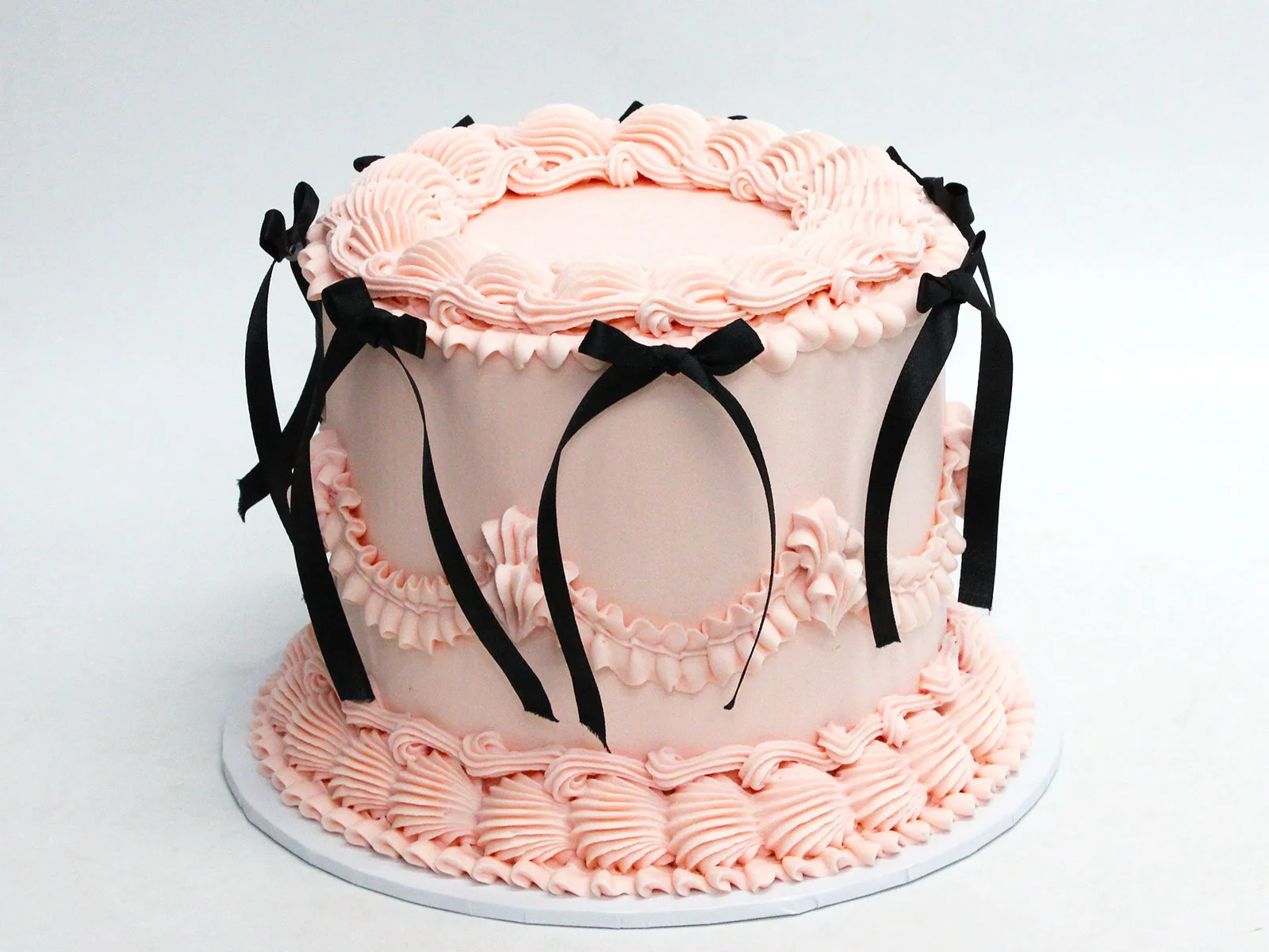 Pink round vintage cake with black ribbon bows and piped borders